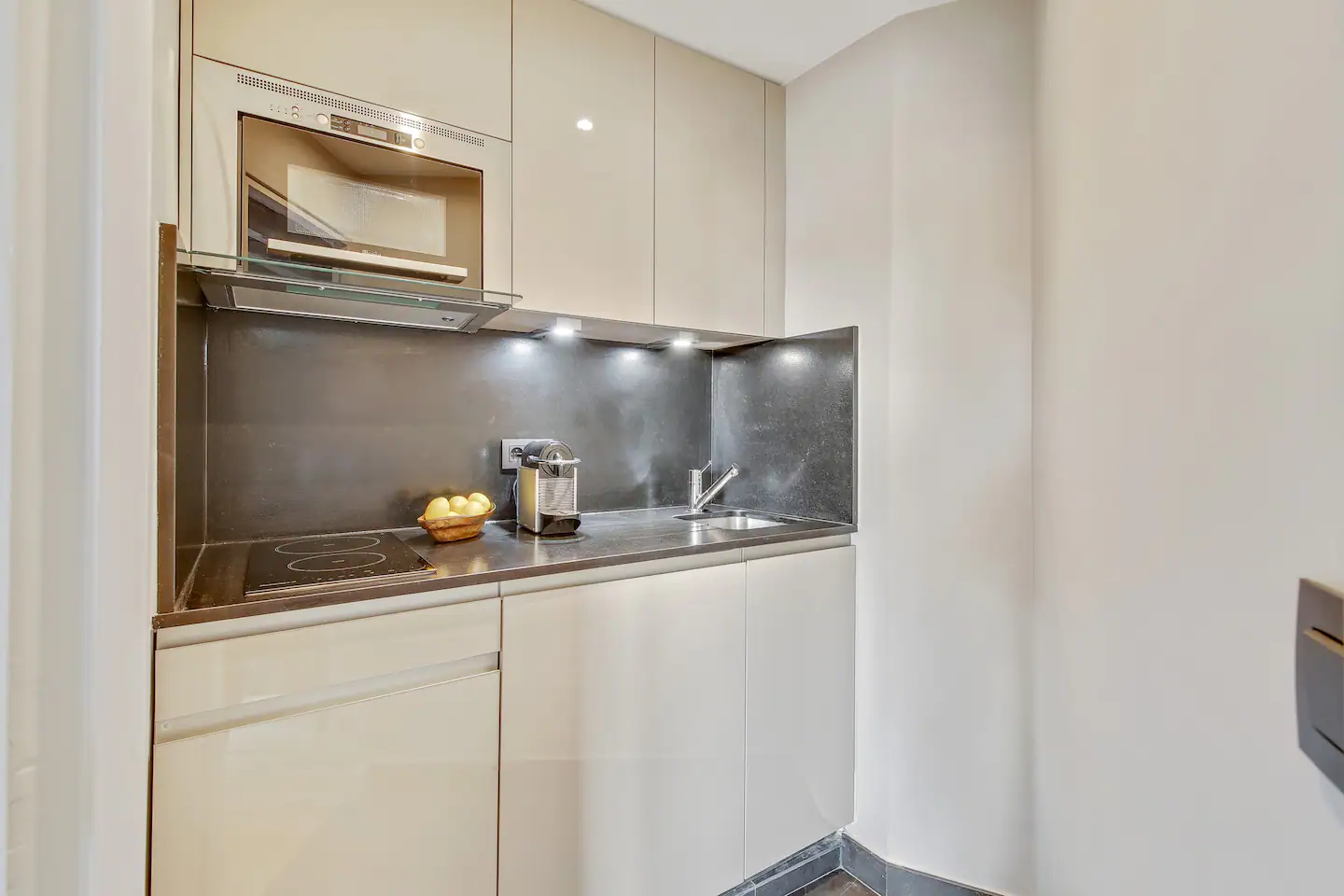 The kitchen has a fridge, stove, microwave, coffee maker, and all the utensils you need, with built-in shelves and a tiled floor.